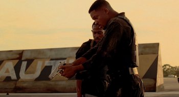 Movie still from “Bad Boys” (1995), directed by Michael Bay – Two men in black uniforms holding a gun and looking at it; Medium shot, Low angle