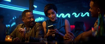 Movie still from “Bad Boys for Life” (2020), directed by Adil El Arbi – A woman looking at her cell phone while sitting at a table; Medium shot, Over the shoulder angle