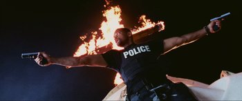 Movie still from “Bad Boys II” (2003), directed by Michael Bay – A man in a police uniform standing in front of a fire; Medium shot, Low angle