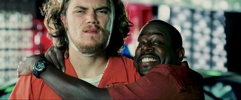 Movie still from “Bad Boys II” (2003), directed by Michael Bay – A man with long hair is hugging another man; Close Up shot, Over the shoulder angle
