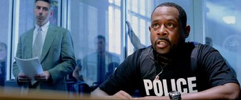 Movie still from “Bad Boys II” (2003), directed by Michael Bay – A man wearing headphones and a police shirt; Close Up shot, Over the shoulder angle
