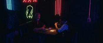 Two men sitting at a table in front of neon lights