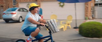 Movie still from “Barb and Star Go to Vista Del Mar” (2021), directed by Josh Greenbaum – A person riding a bike with a basket on the back; Medium shot, Low angle