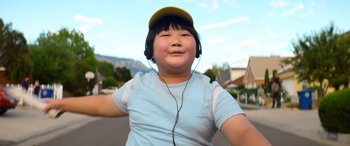 Movie still from “Barb and Star Go to Vista Del Mar” (2021), directed by Josh Greenbaum – A young girl wearing headphones and a yellow hat; Close Up shot, Low angle
