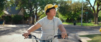 Movie still from “Barb and Star Go to Vista Del Mar” (2021), directed by Josh Greenbaum – A young person riding a bike wearing headphones; Close Up shot, Low angle