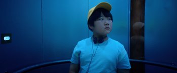 Movie still from “Barb and Star Go to Vista Del Mar” (2021), directed by Josh Greenbaum – A boy with a yellow hat and headphones on; Close Up shot, Low angle