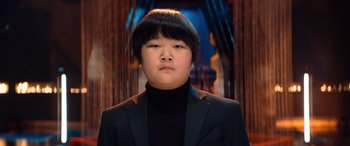 Movie still from “Barb and Star Go to Vista Del Mar” (2021), directed by Josh Greenbaum – A person wearing a black suit and a black jacket; Close Up shot, Low angle