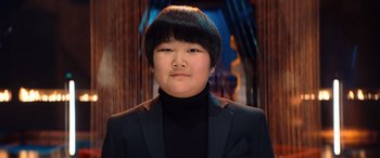 Movie still from “Barb and Star Go to Vista Del Mar” (2021), directed by Josh Greenbaum – A person wearing a black suit and a black jacket; Close Up shot, Low angle