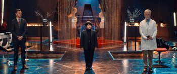 A man in a suit standing in front of a red throne