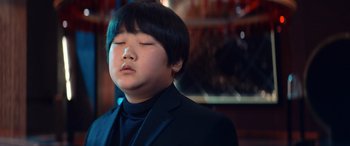 Movie still from “Barb and Star Go to Vista Del Mar” (2021), directed by Josh Greenbaum – A young boy in a black suit and black shirt; Close Up shot, Low angle