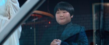 Movie still from “Barb and Star Go to Vista Del Mar” (2021), directed by Josh Greenbaum – A young boy in a black suit is posing for a picture; Close Up shot, Low angle