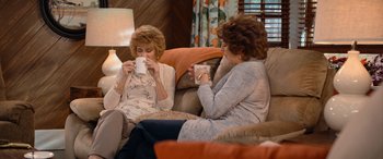 Movie still from “Barb and Star Go to Vista Del Mar” (2021), directed by Josh Greenbaum – Two older women sitting on a couch drinking coffee; Medium shot, High angle