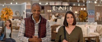 Movie still from “Barb and Star Go to Vista Del Mar” (2021), directed by Josh Greenbaum – A man and a woman posing for a picture in a store; Medium shot, Over the shoulder angle
