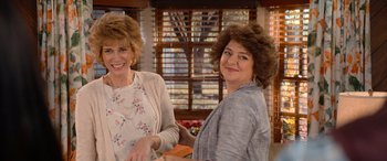 Movie still from “Barb and Star Go to Vista Del Mar” (2021), directed by Josh Greenbaum – Two women standing next to each other in front of a window; Medium shot, Over the shoulder angle