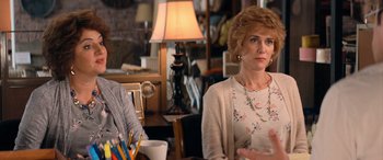Movie still from “Barb and Star Go to Vista Del Mar” (2021), directed by Josh Greenbaum – Two people sitting at a table in front of a lamp; Medium shot, Over the shoulder angle