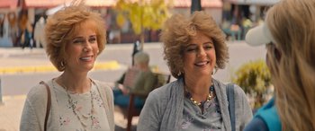 Movie still from “Barb and Star Go to Vista Del Mar” (2021), directed by Josh Greenbaum – Two women are sitting outside and smiling for the camera; Close Up shot, Over the shoulder angle