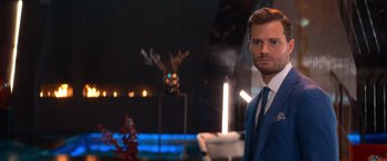 Movie still from “Barb and Star Go to Vista Del Mar” (2021), directed by Josh Greenbaum – A man wearing a suit and tie standing in front of candles; Close Up shot, Over the shoulder angle
