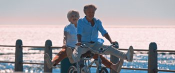 Movie still from “Barb and Star Go to Vista Del Mar” (2021), directed by Josh Greenbaum – An older man and woman riding a bicycle; Wide shot, High angle