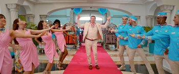 Movie still from “Barb and Star Go to Vista Del Mar” (2021), directed by Josh Greenbaum – A man in a suit and tie standing on a red carpet; Wide shot, Low angle