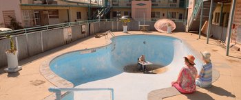 Movie still from “Barb and Star Go to Vista Del Mar” (2021), directed by Josh Greenbaum – A man sitting at a table in a swimming pool; Extreme Wide shot, High angle