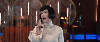 Movie still from “Barb and Star Go to Vista Del Mar” (2021), directed by Josh Greenbaum – A woman in a white dress talking on a phone; Medium shot, Over the shoulder angle