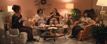 Movie still from “Barb and Star Go to Vista Del Mar” (2021), directed by Josh Greenbaum – A group of people sitting around a glass coffee table; Wide shot, High angle