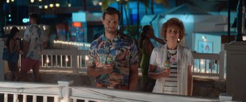 Movie still from “Barb and Star Go to Vista Del Mar” (2021), directed by Josh Greenbaum – A man and a woman standing next to each other holding drinks; Medium shot, Over the shoulder angle