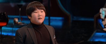 Movie still from “Barb and Star Go to Vista Del Mar” (2021), directed by Josh Greenbaum – A young boy wearing a black jacket and a black shirt; Close Up shot, Low angle