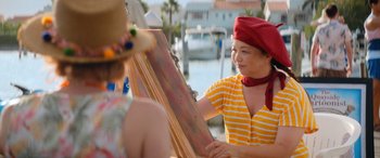 Movie still from “Barb and Star Go to Vista Del Mar” (2021), directed by Josh Greenbaum – A woman wearing a red hat is painting a picture; Close Up shot, Over the shoulder angle