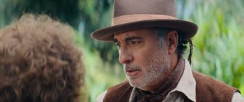 Movie still from “Barb and Star Go to Vista Del Mar” (2021), directed by Josh Greenbaum – An older man wearing a brown hat looking at something; Close Up shot, Over the shoulder angle