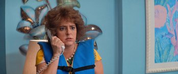 Movie still from “Barb and Star Go to Vista Del Mar” (2021), directed by Josh Greenbaum – A woman wearing a life jacket while talking on the phone; Close Up shot, High angle