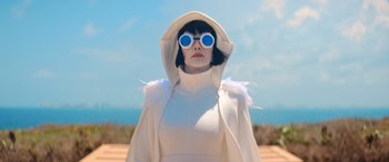 Movie still from “Barb and Star Go to Vista Del Mar” (2021), directed by Josh Greenbaum – A woman wearing a white outfit and blue sunglasses; Medium shot, Low angle