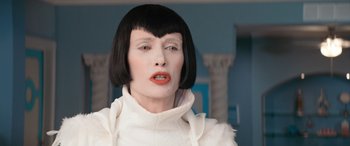 Movie still from “Barb and Star Go to Vista Del Mar” (2021), directed by Josh Greenbaum – A woman with black hair wearing a white outfit; Close Up shot, Low angle