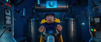 Movie still from “Barb and Star Go to Vista Del Mar” (2021), directed by Josh Greenbaum – A young boy is driving a car in an amusement park; Medium shot, Low angle