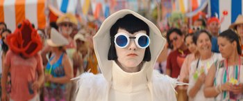 Movie still from “Barb and Star Go to Vista Del Mar” (2021), directed by Josh Greenbaum – A person wearing a white outfit and blue sunglasses; Close Up shot, Over the shoulder angle