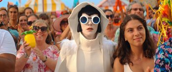 Movie still from “Barb and Star Go to Vista Del Mar” (2021), directed by Josh Greenbaum – A woman in a white outfit and blue sunglasses; Close Up shot, Low angle