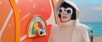 Movie still from “Barb and Star Go to Vista Del Mar” (2021), directed by Josh Greenbaum – A woman in a white coat and white sunglasses standing in front of a meter; Close Up shot, Low angle