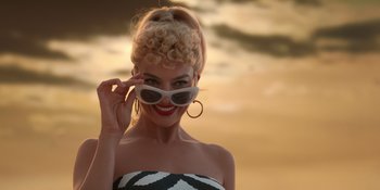 Movie still from “Barbie” (2023), directed by Greta Gerwig – A woman in a black and white striped dress with sunglasses; Close Up shot, Low angle