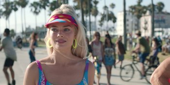 Movie still from “Barbie” (2023), directed by Greta Gerwig – A woman wearing a colorful hat and a colorful dress; Close Up shot, Over the shoulder angle