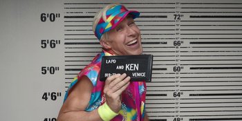 Movie still from “Barbie” (2023), directed by Greta Gerwig – A man in a tie dye outfit holding up a sign; Medium shot, Overhead angle