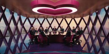 Movie still from “Barbie” (2023), directed by Greta Gerwig – A group of people sitting at a table in a room; Wide shot, High angle
