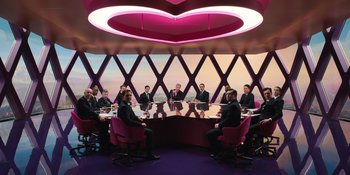 Movie still from “Barbie” (2023), directed by Greta Gerwig – A group of people sitting around a table in a room; Extreme Wide shot, High angle