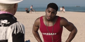 Movie still from “Barbie” (2023), directed by Greta Gerwig – A young man is standing on the beach listening to music; Medium shot, Over the shoulder angle