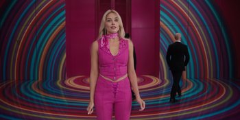 Movie still from “Barbie” (2023), directed by Greta Gerwig – A woman in a pink outfit standing in front of a colorful wall; Medium shot, Low angle