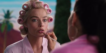 Movie still from “Barbie” (2023), directed by Greta Gerwig – A woman in a pink bathrobe putting lipstick on her lips; Close Up shot, Over the shoulder angle