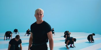 Movie still from “Barbie” (2023), directed by Greta Gerwig – A man standing in front of a group of people; Medium shot, Low angle