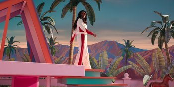 Movie still from “Barbie” (2023), directed by Greta Gerwig – A woman standing on top of a platform in front of palm trees; Extreme Wide shot, Low angle