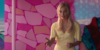 Movie still from “Barbie” (2023), directed by Greta Gerwig – A woman in a yellow dress talking to someone in front of a pink wall; Medium shot, Over the shoulder angle