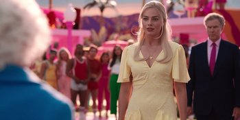 Movie still from “Barbie” (2023), directed by Greta Gerwig – A woman in a yellow dress standing in front of a group of people; Medium shot, Over the shoulder angle