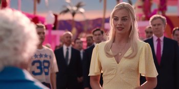 Movie still from “Barbie” (2023), directed by Greta Gerwig – A woman standing in front of a group of people; Close Up shot, Over the shoulder angle